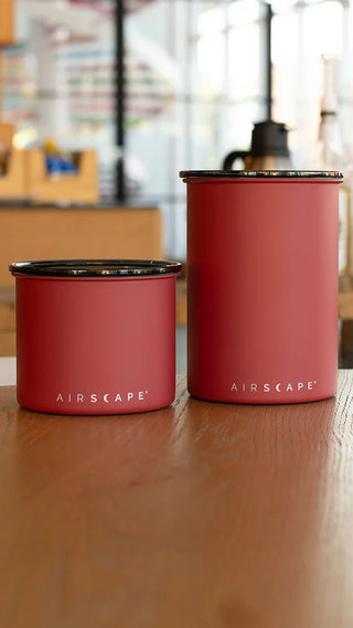 Zwei Airscape Kaffeedosen in Ziegelrot aus Edelstahl auf Holztisch – luftdichte Aufbewahrung für Kaffeebohnen im modernen Küchenambiente