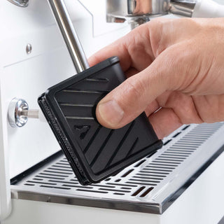Barista hält das Reinigungswerkzeug von Artpresso und reinigt die Dampfdüse einer Espressomaschine.