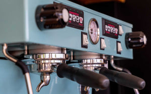 Nahaufnahme einer türkisfarbenen Espressomaschine mit eingespannten Siebträgern.