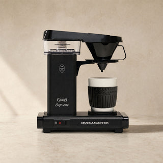 Moccamaster Cup One in Matt Black auf Küchenarbeitsplatte, Filterkaffeemaschine mit Tasse in warmer Umgebung
