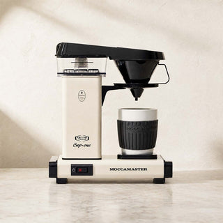 Moccamaster Cup One in Off White auf Küchenarbeitsplatte, Filterkaffeemaschine mit Tasse in warmer Umgebung