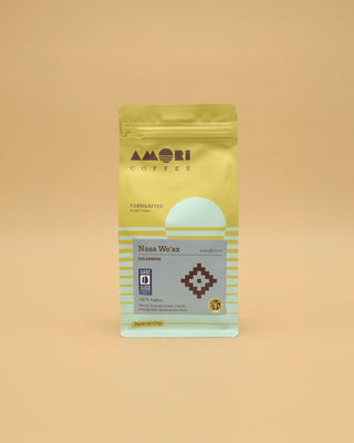 AMORI Coffee Nasa We’sx, entkoffeinierter Farmkaffee aus Kolumbien mit 100 % Arabica, in gelber Kaffeeverpackung mit hellblauen Streifen, graublauem Produktetikett, dunkelbraunem geometrischem Rautensymbol und Siegeln von Clean Coffee Clean Ocean und Rainforest Alliance.