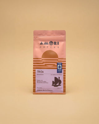 AMORI Coffee Vela Espresso-Blend aus 80 % Arabica und 20 % Robusta in rosa-orangefarbener Kaffeeverpackung mit violettem Etikett, Segelschiff-Symbol und Clean-Ocean-Siegel.