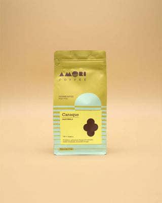 AMORI Coffee Canaque Farmkaffee aus Guatemala, 100 % Arabica, in gelb-grüner Kaffeeverpackung mit hellblauen Streifen, gelbem Produktetikett und dunkelbraunem, vierblättrigem Symbol.