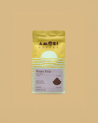 AMORI Coffee Hoyo Frío Farmkaffee aus Kolumbien, 100 % Arabica aus Direct Trade, in gelber Kaffeeverpackung mit hellblauen Streifen, lilafarbenem Produktetikett und dunkelbraunem geometrischem Symbol.