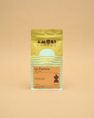 AMORI Coffee La Pastora Farmkaffee aus Costa Rica, 100 % Arabica, in gelber Kaffeeverpackung mit hellblauen Streifen, orangefarbenem Produktetikett und dunkelbraunem geometrischem Symbol.
