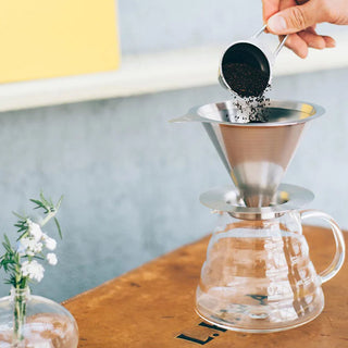 Gemahlener Kaffee wird in einen Hario V60 Edelstahl-Filter über einer Glaskaraffe eingefüllt.