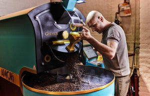 Das Foto zeigt Roberto Cascone, den Inhaber von AMORI Coffee, der die Röstanlage in der Rösterei bedient. Frisch gerösteter Kaffee läuft auf die Trommel des Rösters. 