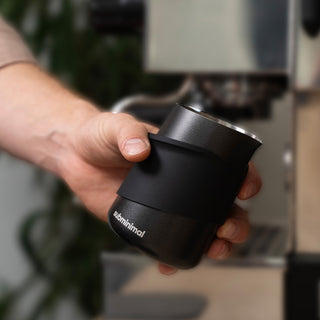 Hand hält den Subminimal Subscale Digital Dosing Cup vor einer Siebträgermaschine – Fokus auf Haptik und kompaktes Design.